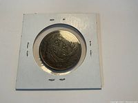 Obverse side of the 1837 Canada Bank token showing shield with quartered emblem and inscriptions including "ONE PENNY." Coin mounted in white cardboard holder.