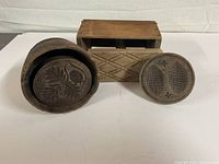 Photo showing the three antique wooden butter presses side by side: rectangular with handle, round with leaf carving, and small decorative round press.