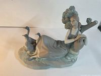 Front-left angled view showing lady reclining with three geese and tree backdrop.