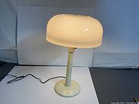 Front view of the lit desk lamp showing mushroom-shaped white shade and cylindrical base.