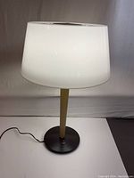 MCM Gerald Thurston table lamp front and side view showing white opaque glass shade, wood stem, black circular base, and cord with switch.