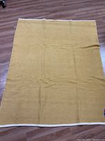 Top view of mustard yellow blanket with cream border on wooden floor.