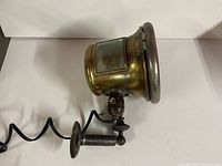 Side view of brass headlight showing coiled electrical cord and mounting bracket attached to the base.