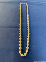 Full length photo of the pearl necklace carefully laid out on a blue background showing the full strand of round white pearls.
