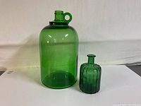Photo of a large green glass jug beside a smaller green glass bottle, showing shape and relative size.