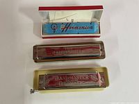 Top view of three harmonicas: Blessing blue harmonica in box with cloth, Band Master harmonica, and Band Master De Luxe Chromatic Seydels System harmonica.