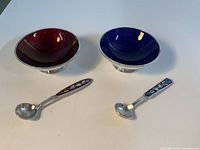 Two enamel open salt bowls, red and blue, with matching spoons shown from above.