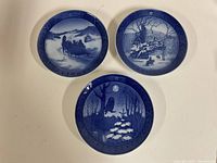 Top view of three vintage Royal Copenhagen collector plates showing blue and white winter scenes dated 1964, 1967, and 1974.