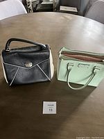 Two Kate Spade handbags side by side on a table, one black with white piping and one mint green tote.