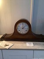 Full view of wooden mantel clock with winding key and paper displayed on marble shelf.