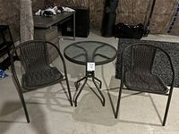 Photo of a small bistro set with 2 chairs and a round glass top table in a storage setting.