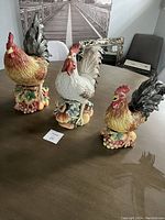 Three Fritz and Floyd ceramic rooster figurines displayed on table in natural lighting, showing full front view of each piece.
