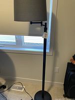 Full view of black floor lamp with dark grey shade near a window, showing the swivel arm and shade.