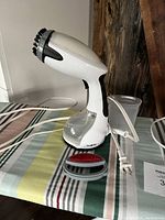 Handheld steamer with transparent water container and power cord, placed on striped ironing board