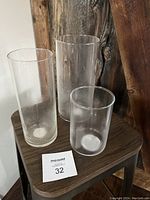 Three clear glass cylinder vases in varying sizes on wooden stool