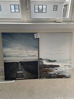 Two ocean scene prints leaning against wall showing one with path to beach and the other with rocky coastline and ocean waves