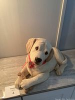 Front side view of the Sandicast life size Yellow Labrador puppy figurine on a countertop, showing the face, red collar and toy bone held in paws.