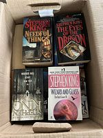 Box containing paperback Stephen King books including 'Needful Things', 'The Eyes of the Dragon', 'Wizard and Glass', and 'The Girl Who Loved Tom Gordon'.