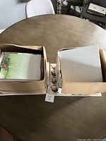 Two cardboard boxes on a round table containing various paper products and notebooks