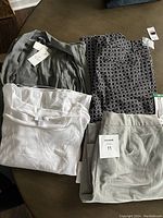 Four clothing items: white shirt, checkered pants, grey pants, and grey sweater with tags