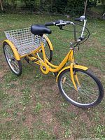 Full side view of yellow adult tricycle showing frame, wheels, basket, saddle and handlebars