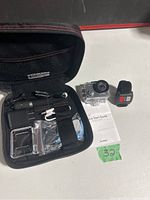 Overview of the AKASO V50X action camera and its accessories arranged around a black carrying case. Visible are the camera in waterproof case, remote control, charger, USB cable, and quick start guide.