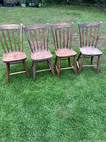 Front view of four matching antique wooden chairs showing spindle backs and carved wooden seats in used condition.