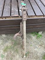 Full view of the antique cast iron water pump standing upright with partial wooden handle attached, placed outdoors on the ground near wooden decking.