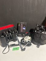 Overview of Skyline binoculars with case, Morphie phone charger box, Bushnell digital binoculars, and Nikon Coolpix camera with strap.