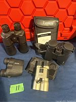 Photo showing all four binoculars with Ecokra branded carrying case and instruction manual and green marker labeled "11"