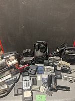 Overview of lot showing cameras, camcorders, chargers, batteries and cases on table