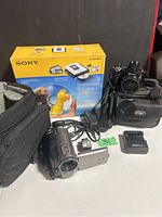 Photo of Panasonic Palmsight camcorder, Nikon camera, Sony DVD recorder box and devices all arranged on table.
