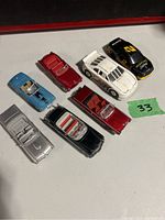 Seven collectible diecast cars arranged on a flat surface, showing various colors and styles including convertibles and race cars.