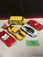 Top-down view of five diecast vehicles including the yellow Michelin Van and three sports cars on a black surface with a green sticker number 34.