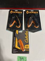 Lot showing two Gerber Profile folding knives and one Cabela's folding knife in original packaging.