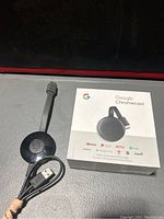 Image of used Google Chromecast device with HDMI cable and USB power cable on surface.