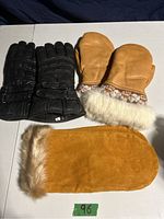 Photo showing the black leather Thinsulate lined gloves size small, tan leather mittens with embroidered Huron moccasin cuff and white fur trim, and an additional tan suede mitten with fur trim.