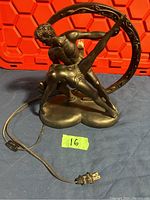Black oxide metal lamp with intertwined two male figure sculpture on base, visible power cord and plug, showing front and side profile
