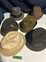 Photo showing six vintage men's felt hats in various earth tones and one beige fur-like hat, arranged on a white surface.