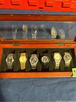 Wooden watch display case with six watches on black cushions seen from above through glass lid
