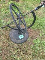 Full view of cast iron sundial showing circular dial with Roman numerals and arrow-shaped gnomon, positioned on grass.
