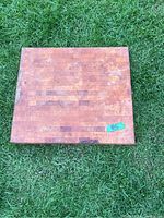 Top view of one thick wooden butcher block on grass, showing rectangular wood block patterns and signs of wear.