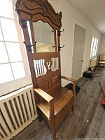 Angled front view showing carved crest, mirror, hooks and storage seat.