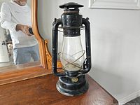 Full view of the black antique lantern placed on a wooden surface with a mirror in the background.