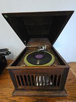 Front view of antique wooden phonograph cabinet with lid open revealing turntable and record on it.