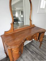 Side angled view showing curved wooden top, attached mirror, and side cabinet door details