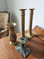 Photo showing four candle holders on a wooden surface near a chair and a mirror.