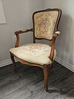 Front view of wooden armchair with carved arms and legs, tapestry upholstery on backrest and seat showing floral and romantic couple design.