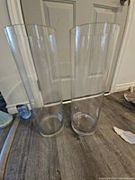 Photo showing the two tall clear glass vases standing side by side in front of a door, showing their height and transparency.