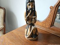 Front view of the wooden Rastafarian carving, showing the figure sitting and holding a pipe and bowl.
